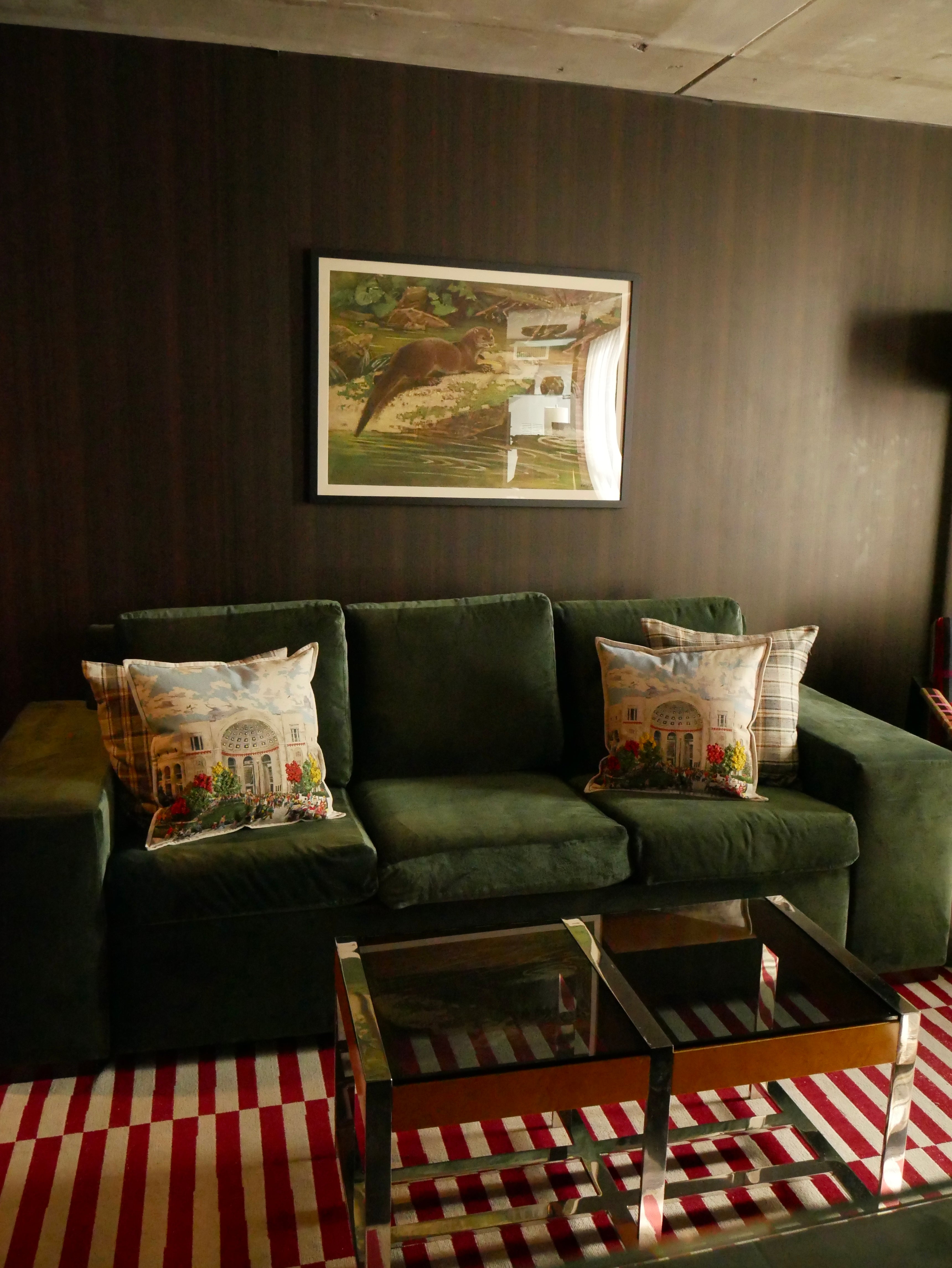 Green sofa with patterned cushions in a room with a dark wall and framed picture.